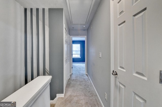 hallway with light colored carpet, attic access, and baseboards