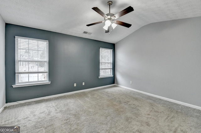 carpeted empty room featuring a wealth of natural light, visible vents, baseboards, and vaulted ceiling