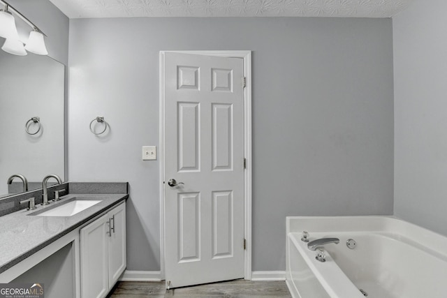 bathroom featuring baseboards, vanity, a garden tub, wood finished floors, and a textured ceiling