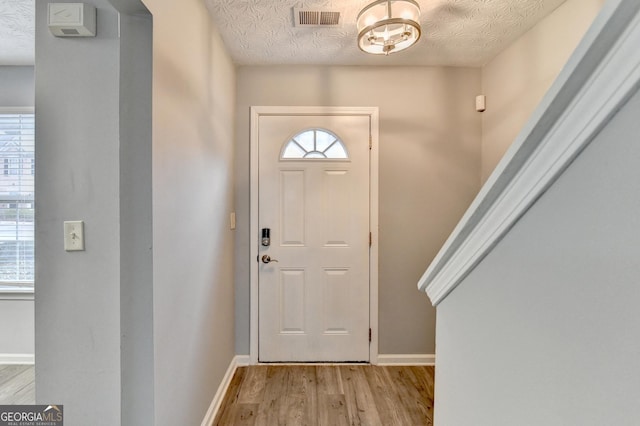 foyer entrance with baseboards, visible vents, a textured ceiling, and light wood-style floors