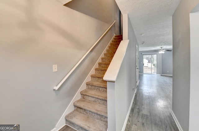 stairway featuring a ceiling fan, wood finished floors, baseboards, and a textured ceiling