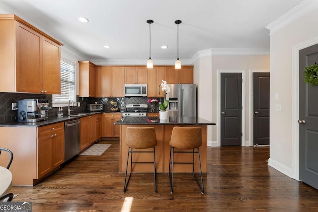 kitchen with a sink, appliances with stainless steel finishes, a center island, dark countertops, and dark wood finished floors