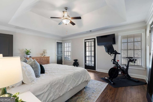 bedroom featuring wood finished floors, visible vents, baseboards, ornamental molding, and a tray ceiling