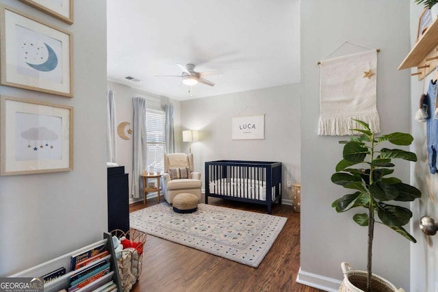 bedroom featuring baseboards, visible vents, a ceiling fan, wood finished floors, and a nursery area