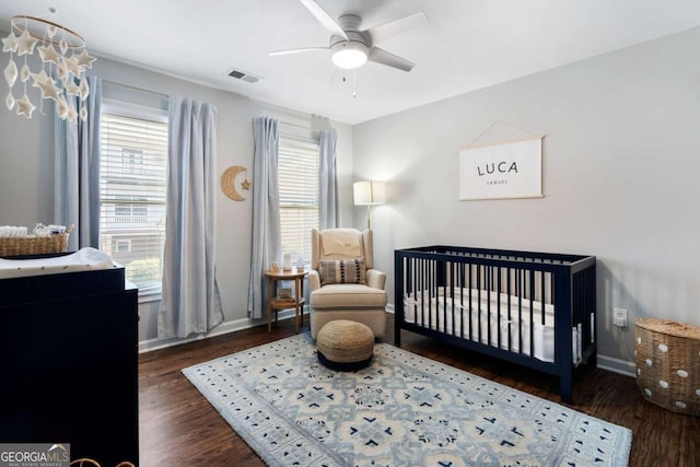 bedroom with visible vents, a crib, baseboards, and wood finished floors