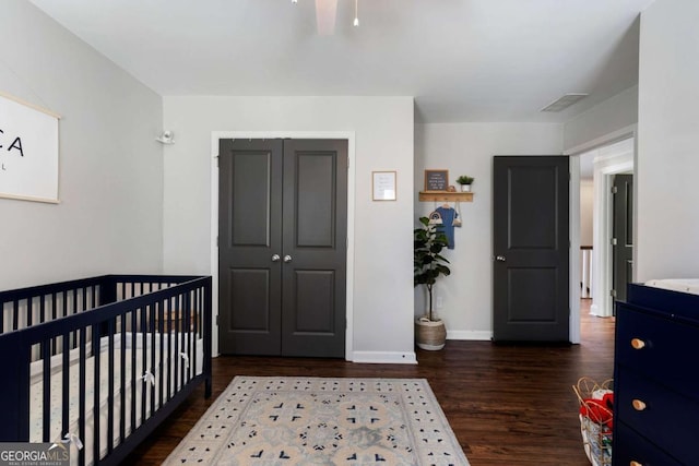 bedroom with a crib, baseboards, visible vents, wood finished floors, and a closet