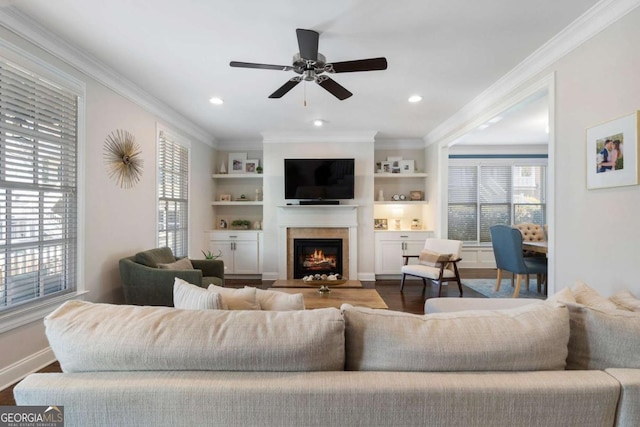 living room featuring a warm lit fireplace, built in shelves, ornamental molding, and wood finished floors