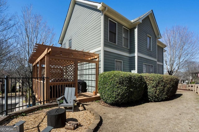 rear view of house featuring a deck, fence, and a pergola