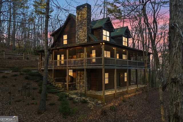 back of house at dusk with a patio area, a chimney, stone siding, and a wooden deck