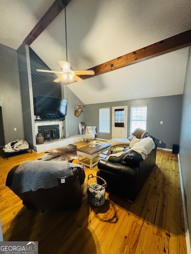 living room featuring vaulted ceiling with beams, hardwood / wood-style floors, a textured ceiling, and a brick fireplace