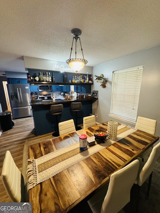 dining room with a textured ceiling, bar area, and wood finished floors