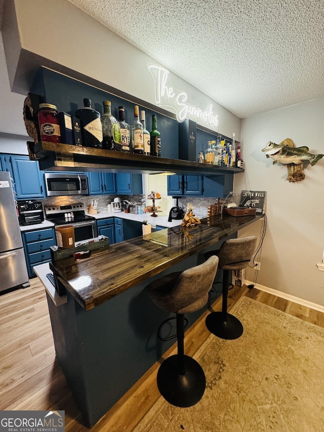 bar featuring light wood finished floors, appliances with stainless steel finishes, a textured ceiling, and wet bar