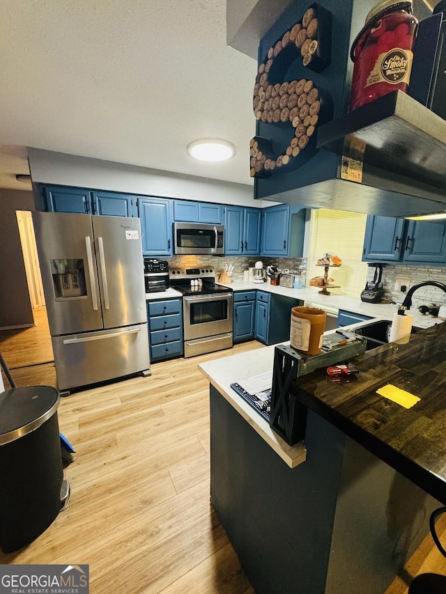 kitchen with tasteful backsplash, appliances with stainless steel finishes, a sink, blue cabinets, and light wood-type flooring