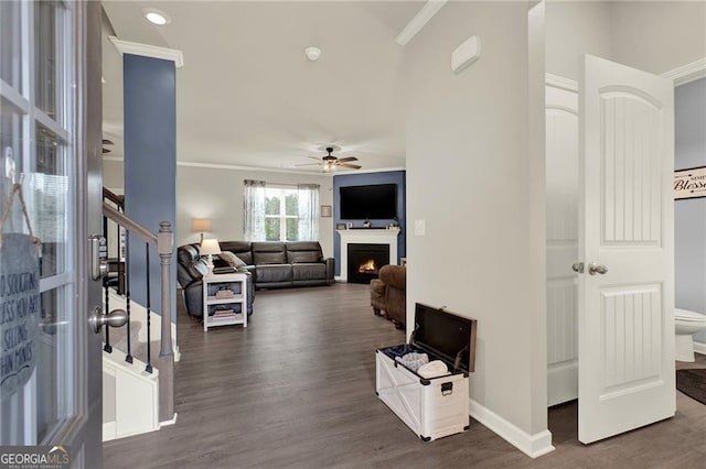 living area with baseboards, ceiling fan, stairway, dark wood-style flooring, and a lit fireplace