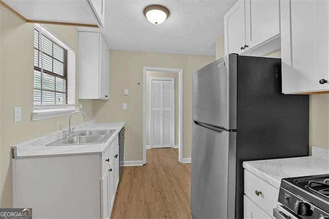 kitchen with light countertops, freestanding refrigerator, a sink, and white cabinetry