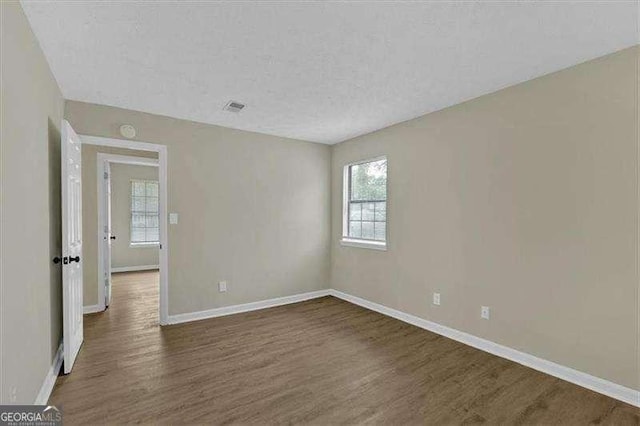 unfurnished room featuring visible vents, a textured ceiling, baseboards, and dark wood-type flooring