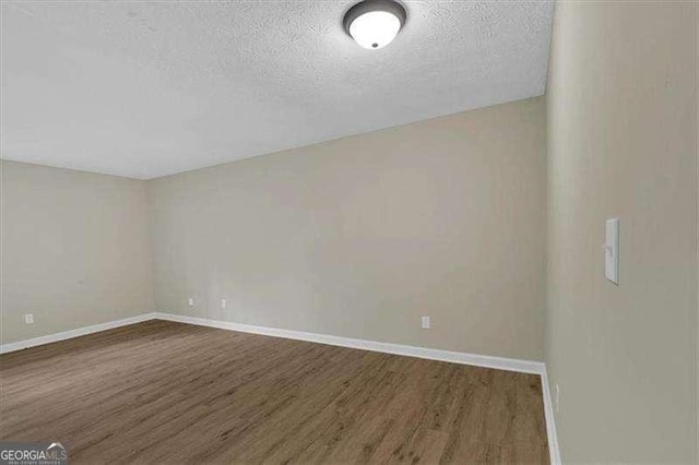 unfurnished room with a textured ceiling, baseboards, and wood finished floors