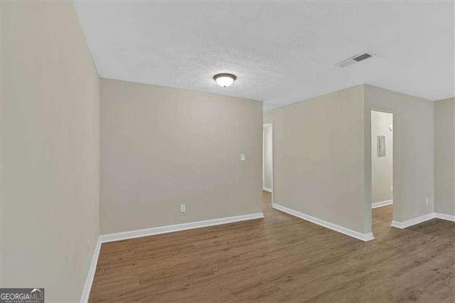 spare room featuring baseboards, a textured ceiling, visible vents, and wood finished floors