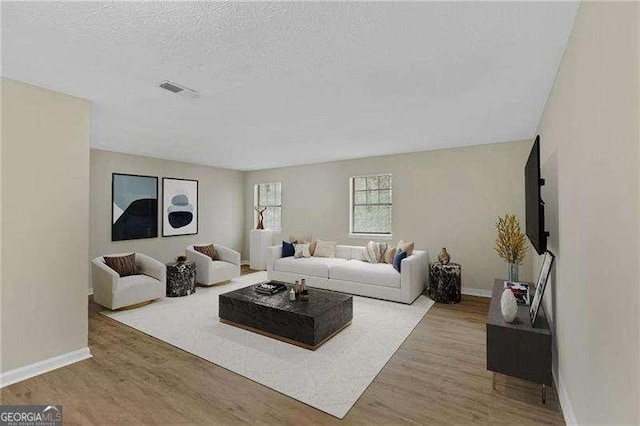 living room featuring visible vents, a textured ceiling, baseboards, and wood finished floors