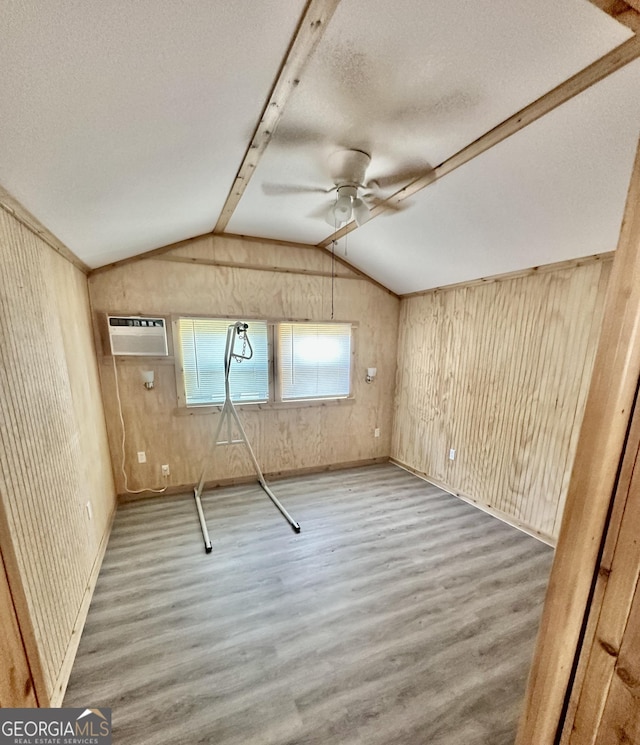 interior space with ceiling fan, wooden walls, wood finished floors, and a wall mounted air conditioner