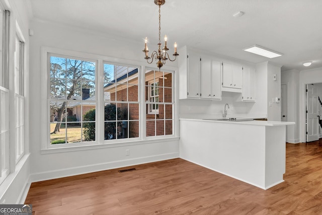 kitchen with baseboards, white cabinets, light wood-style flooring, an inviting chandelier, and light countertops