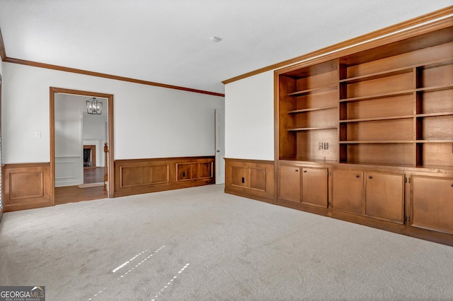 unfurnished living room with built in shelves, a fireplace, carpet flooring, wainscoting, and crown molding