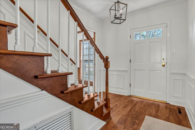 entrance foyer featuring a wainscoted wall, a notable chandelier, crown molding, stairway, and wood finished floors