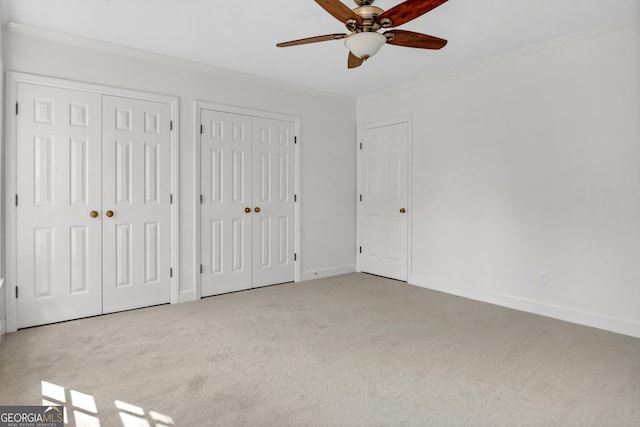 unfurnished bedroom featuring baseboards, ornamental molding, multiple closets, and carpet flooring