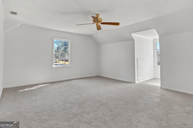 spare room featuring ceiling fan, a textured ceiling, carpet flooring, visible vents, and vaulted ceiling