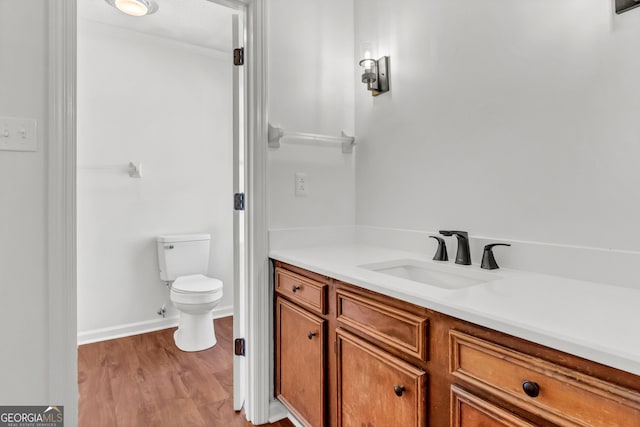 bathroom featuring toilet, baseboards, wood finished floors, and vanity