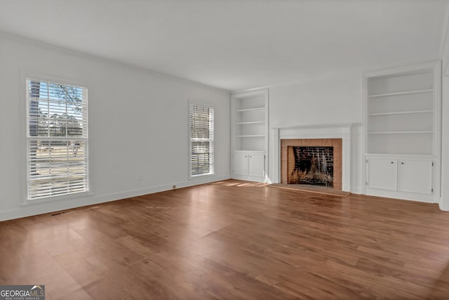 unfurnished living room with baseboards, a fireplace, wood finished floors, and built in features