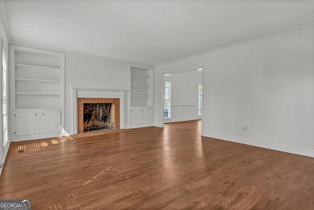 unfurnished living room with baseboards, wood finished floors, crown molding, a brick fireplace, and built in shelves