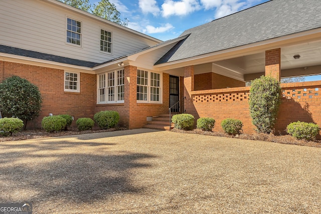 exterior space with brick siding and roof with shingles