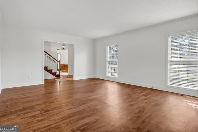 unfurnished living room with stairs, baseboards, and wood finished floors