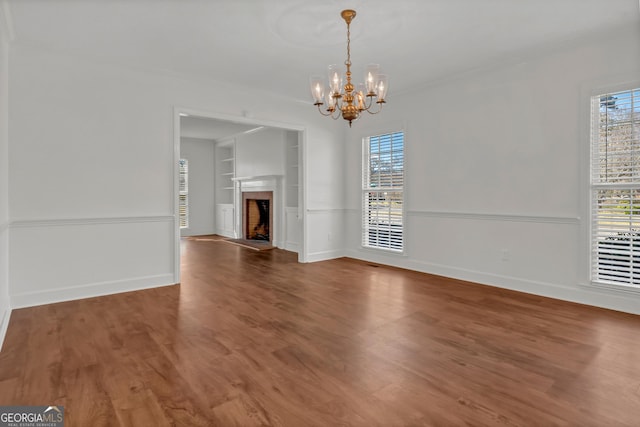 unfurnished dining area with built in features, a fireplace, baseboards, and wood finished floors