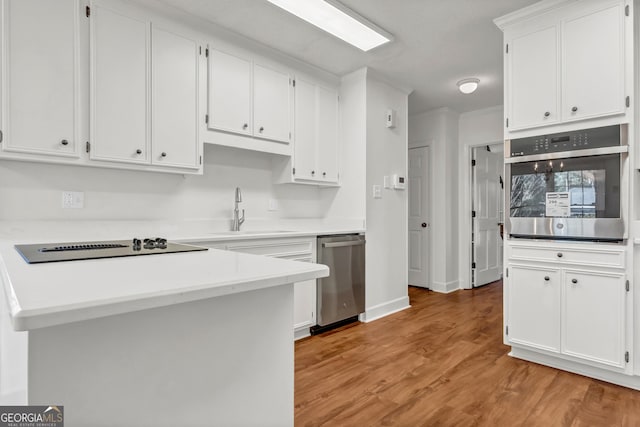 kitchen featuring stainless steel appliances, a sink, white cabinetry, light countertops, and light wood finished floors