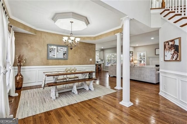 dining space featuring ornate columns, wood finished floors, wainscoting, and a decorative wall