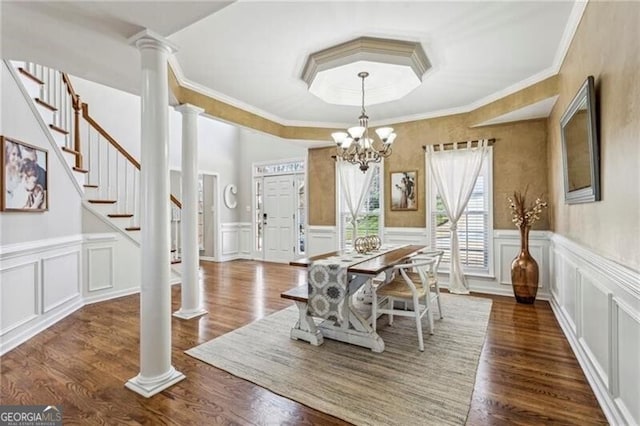 dining area featuring crown molding, a decorative wall, ornate columns, wood finished floors, and a notable chandelier