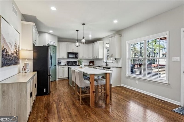 kitchen featuring black microwave, light countertops, dark wood-style flooring, and freestanding refrigerator