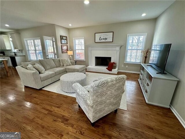living room with dark wood-style flooring, recessed lighting, a brick fireplace, and a wealth of natural light
