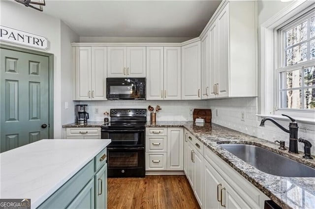 kitchen featuring dark wood-style flooring, light stone counters, white cabinetry, black appliances, and a sink