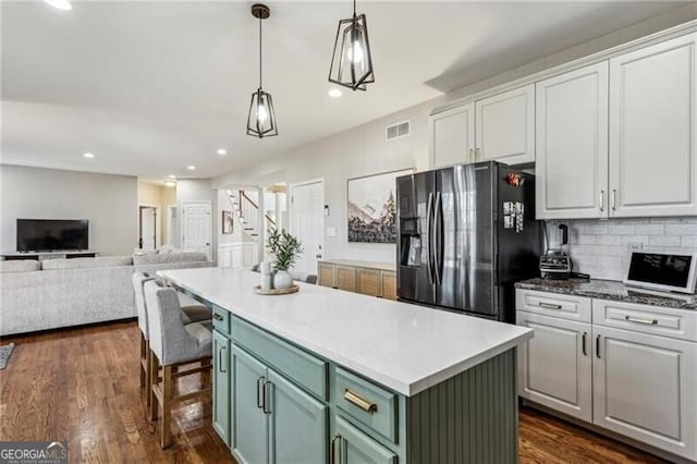 kitchen with white cabinets, visible vents, black fridge, open floor plan, and dark wood-style floors