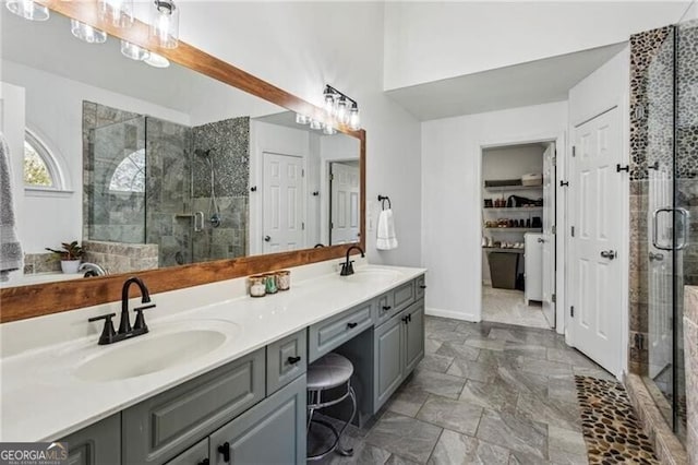 full bath featuring baseboards, double vanity, a sink, and a shower stall