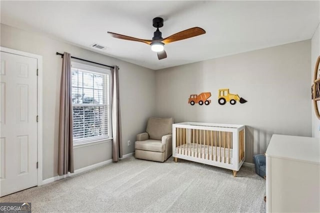 carpeted bedroom featuring a ceiling fan, a nursery area, visible vents, and baseboards