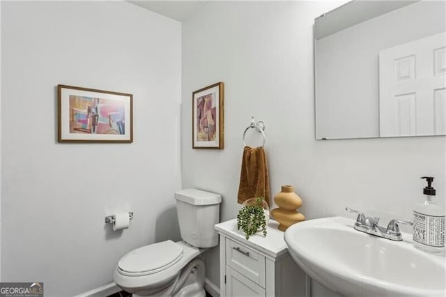 half bath with baseboards, a sink, and toilet