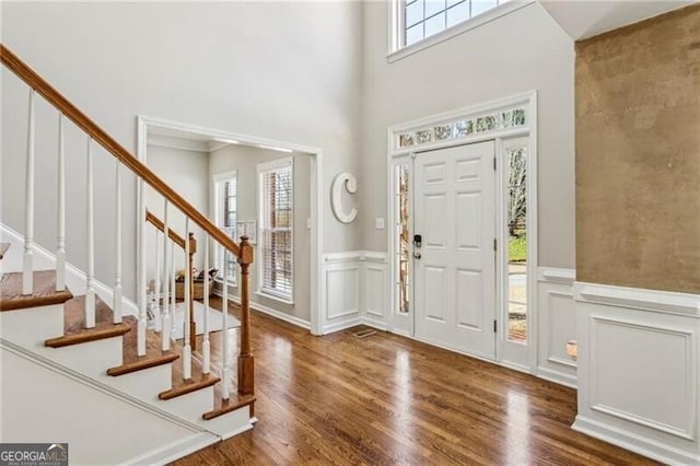 entryway featuring a wainscoted wall, a decorative wall, a towering ceiling, wood finished floors, and stairs