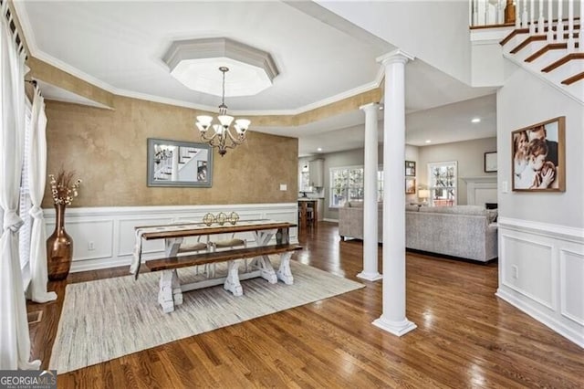 dining space with ornate columns, ornamental molding, wood finished floors, and a wainscoted wall