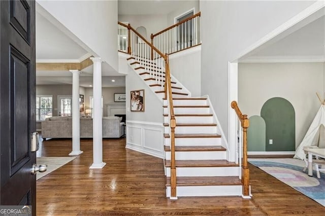 stairway with decorative columns, a towering ceiling, ornamental molding, and wood finished floors