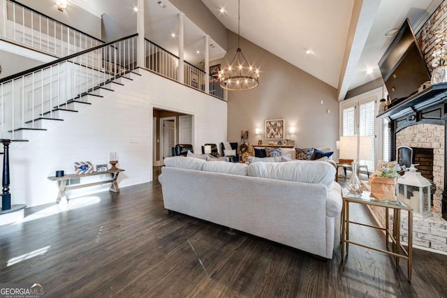 living room featuring wood finished floors, stairs, a high ceiling, a brick fireplace, and a notable chandelier