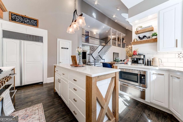 kitchen featuring white cabinets, dark wood-style floors, stainless steel microwave, a warming drawer, and open shelves